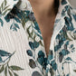 Close-up detail of the crinkle-textured fabric and white buttons of the botanical print shirt.