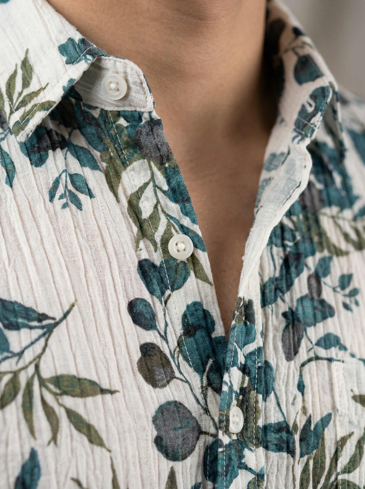 Close-up detail of the crinkle-textured fabric and white buttons of the botanical print shirt.