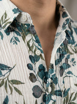 Close-up detail of the crinkle-textured fabric and white buttons of the botanical print shirt.